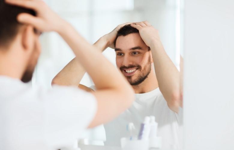 A happy young man styles his hair in front of a mirror.