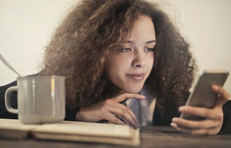 Woman thinking whether to send a text message while leaning on a dark wooden table.
