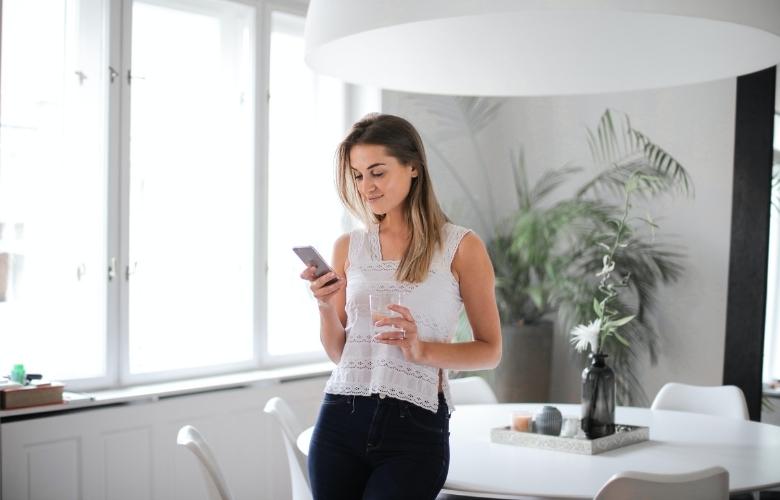Woman wearing a white tank top and blue jeans confidently typing a text message